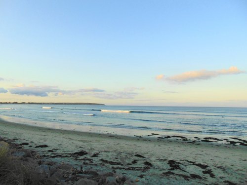 A serene beach scene with gentle waves, sandy shore, and a clear sky with scattered clouds.