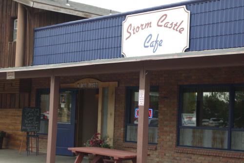 Exterior of Storm Castle Cafe, featuring a blue sign, brick facade, and a picnic table in front.