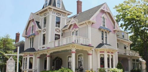 Victorian-style house with a turret, pink accents, and a welcoming porch surrounded by greenery.