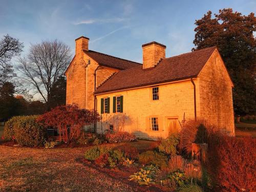 A stone house bathed in golden sunset light, surrounded by colorful gardens and trees.
