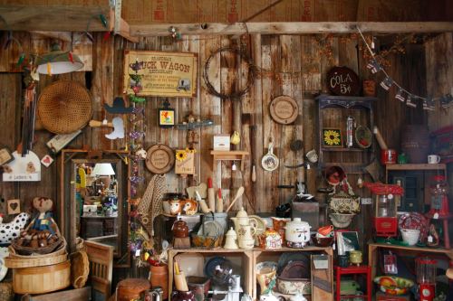 A cozy, rustic interior filled with vintage items, shelves, and decorations against a wooden wall.