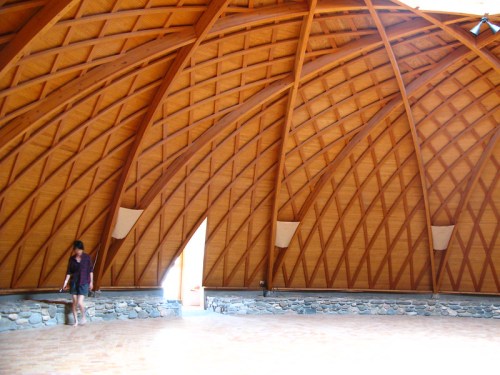 Interior of a spacious wooden structure with a high, vaulted ceiling and a person walking on the floor.