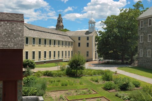 A sunny view of a historic building complex with gardens and a clock tower in the background under a blue sky.