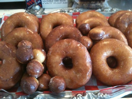 A tray of glazed donuts, featuring large ring-shaped donuts and smaller donut holes, arranged on a red and white checkered paper.