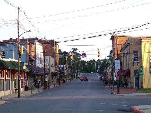 A quiet street in a small town, lined with shops and buildings, with traffic lights and power lines overhead.