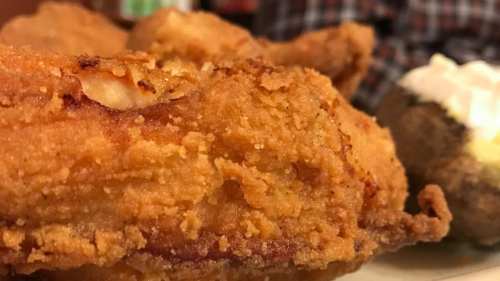 Close-up of crispy fried chicken with a baked potato in the background.