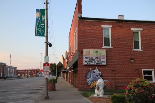 A brick building with a sign, a large mural of a squirrel, and a white statue in a quiet street in Olney.