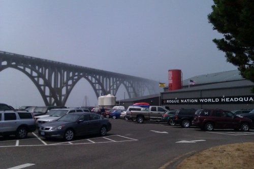 A foggy scene featuring a large bridge above a parking lot filled with cars near a building labeled "Rogue Nation World Headquarters."