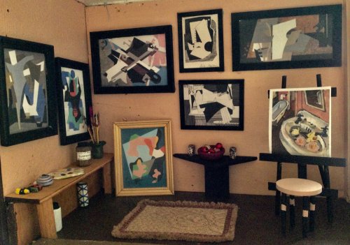 A miniature art studio with framed abstract paintings, a small table with art supplies, and a stool in a cozy setting.