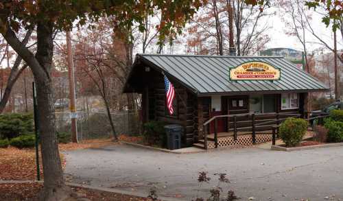 A small log cabin building with a sign, American flag, and autumn foliage surrounding it.