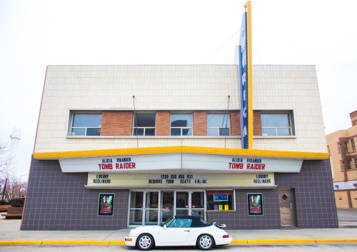 A vintage movie theater featuring a "Tomb Raider" marquee and a white convertible parked outside.