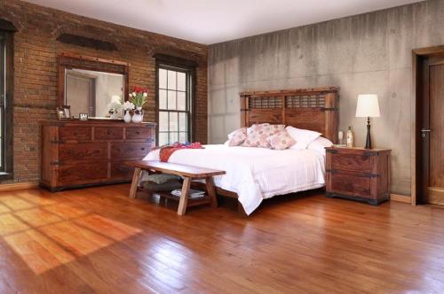 Cozy bedroom featuring a wooden bed, dresser, and nightstand, with brick and concrete walls and warm wooden flooring.