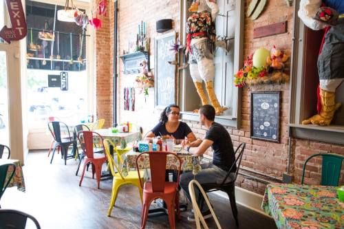 Two people sit at a colorful table in a quirky restaurant with eclectic decor and a cozy atmosphere.