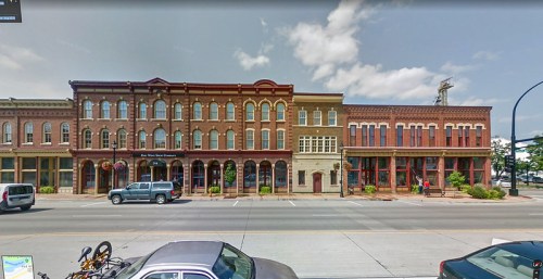 Historic brick buildings line a street, featuring large windows and a clear blue sky above.