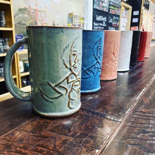 A row of colorful ceramic mugs with intricate designs, displayed on a wooden counter.