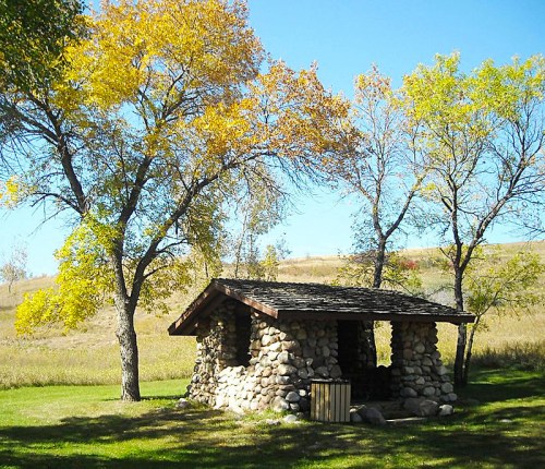 A small stone shelter surrounded by trees with autumn foliage under a clear blue sky.