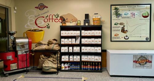 A cozy coffee shop interior featuring a coffee roaster, shelves of coffee bags, and a roasting process chart on the wall.
