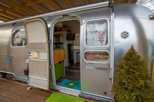 A shiny silver Airstream trailer with an open door, revealing a cozy interior and a small green plant outside.