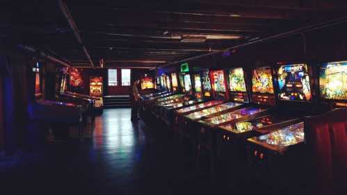 A dimly lit arcade featuring rows of colorful pinball machines.