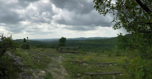 A scenic view of rolling hills under a cloudy sky, with wooden benches arranged in a natural setting.