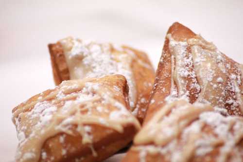 Three golden pastries dusted with powdered sugar and drizzled with icing, arranged on a light background.