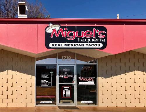 Exterior of Miguel's Taqueria, featuring a sign that reads "Real Mexican Tacos" and an open door.