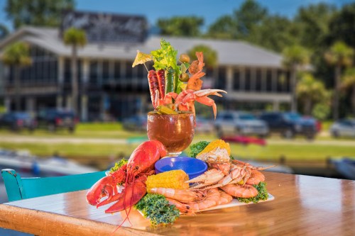 A seafood platter featuring shrimp, lobster, and a cocktail, set on a table with a blurred restaurant in the background.