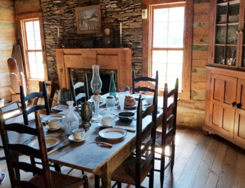 A rustic dining room with a wooden table set for a meal, surrounded by chairs and a stone fireplace.