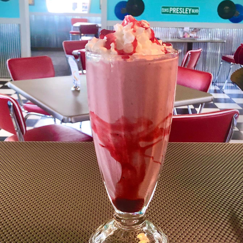 A tall glass of strawberry milkshake topped with whipped cream and cherry, set in a retro diner.