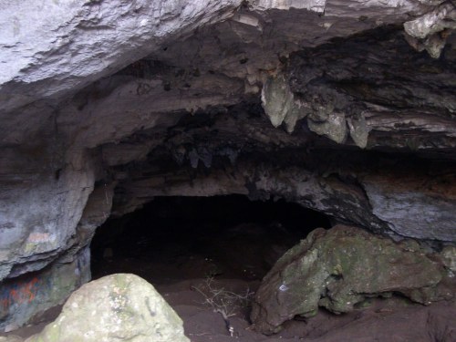 A dark cave interior with rocky walls and stalactites, featuring scattered stones on the ground.