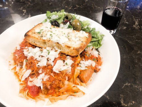 A plate of pasta with marinara sauce, topped with cheese and herbs, served with a slice of toasted bread and a glass of red wine.