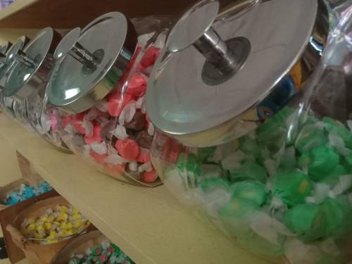 Colorful candy jars filled with assorted sweets, lined up on a shelf with shiny metal lids.