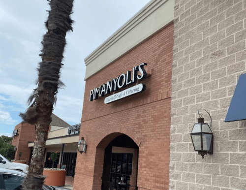 Sign for PimanYoli's, a restaurant, on a brick building with palm trees in the foreground.