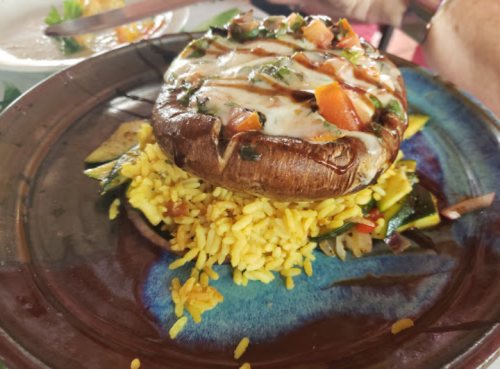 A large stuffed mushroom topped with vegetables and sauce, served on a bed of yellow rice and garnished with herbs.