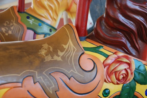 Close-up of a colorful carousel horse's saddle, featuring intricate designs and a rose motif.