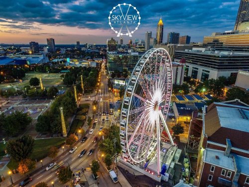 Aerial view of SkyView Atlanta, a large Ferris wheel, with city skyline and colorful sunset in the background.