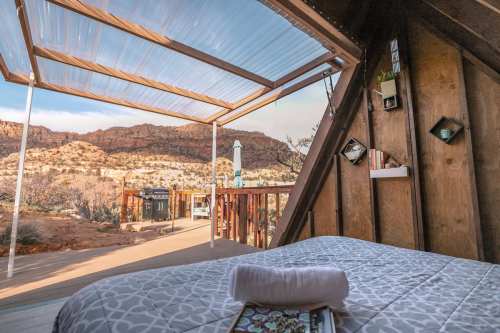 Cozy interior of a cabin with a bed, showcasing a scenic view of mountains through a large window.