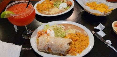 A table setting with two plates of Mexican food, including a burrito, rice, beans, and a margarita drink.