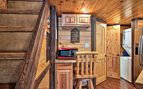 Cozy wooden kitchen with a microwave, bar stool, and staircase, featuring warm lighting and rustic decor.