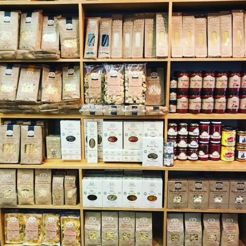 A wooden shelf filled with various pasta packages and jars of sauces, showcasing a variety of colors and designs.