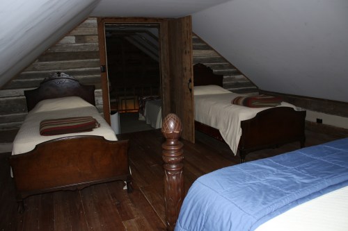 A cozy attic bedroom with two wooden beds, sloped ceilings, and rustic wooden walls.