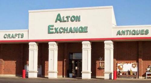 Exterior of Alton Exchange building with signs for crafts and antiques, featuring columns and a clear blue sky.