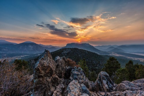 A stunning sunset over mountains, with rays of light breaking through clouds and illuminating the landscape.
