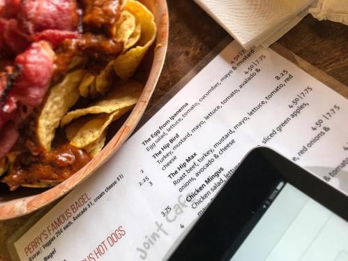 A bowl of nachos with meat beside a menu featuring various food items and a tablet on a table.