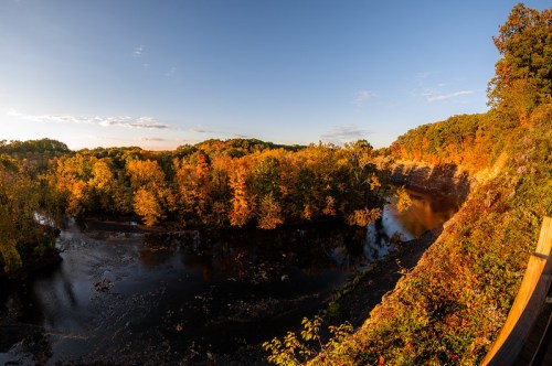 A panoramic view of a river surrounded by vibrant autumn foliage under a clear blue sky.