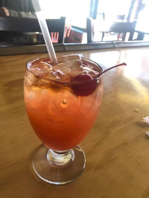 A refreshing cocktail with ice, a cherry on top, served in a clear glass on a wooden table.