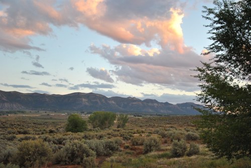 A scenic landscape featuring mountains, clouds, and greenery under a colorful sky at dusk.