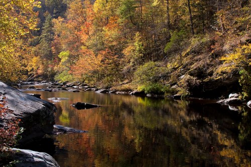 A serene river scene surrounded by vibrant autumn foliage and rocky banks, reflecting colorful trees in the water.