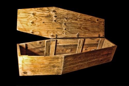 An open wooden coffin with a simple design, resting against a black background.