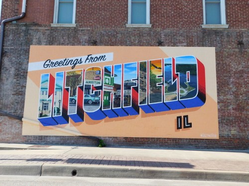 Colorful mural reading "Greetings from Litchfield, IL" on a brick wall, showcasing local landmarks and scenery.